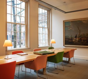 Een lege Studiezaal in het Regionaal Archief Dordrecht. Er staat een tafel met een map er op, de stoelen zijn  rood, oranje en groen.