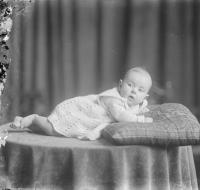 Een baby ligt op de buik op een tafel met een kussen.