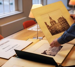 Een man pakt uit een map een oude foto van een gebouw in Dordrecht.