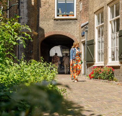 Vrouw in kleurige outfit met spijkerjasje loopt in de richting van Hof van Nederland.